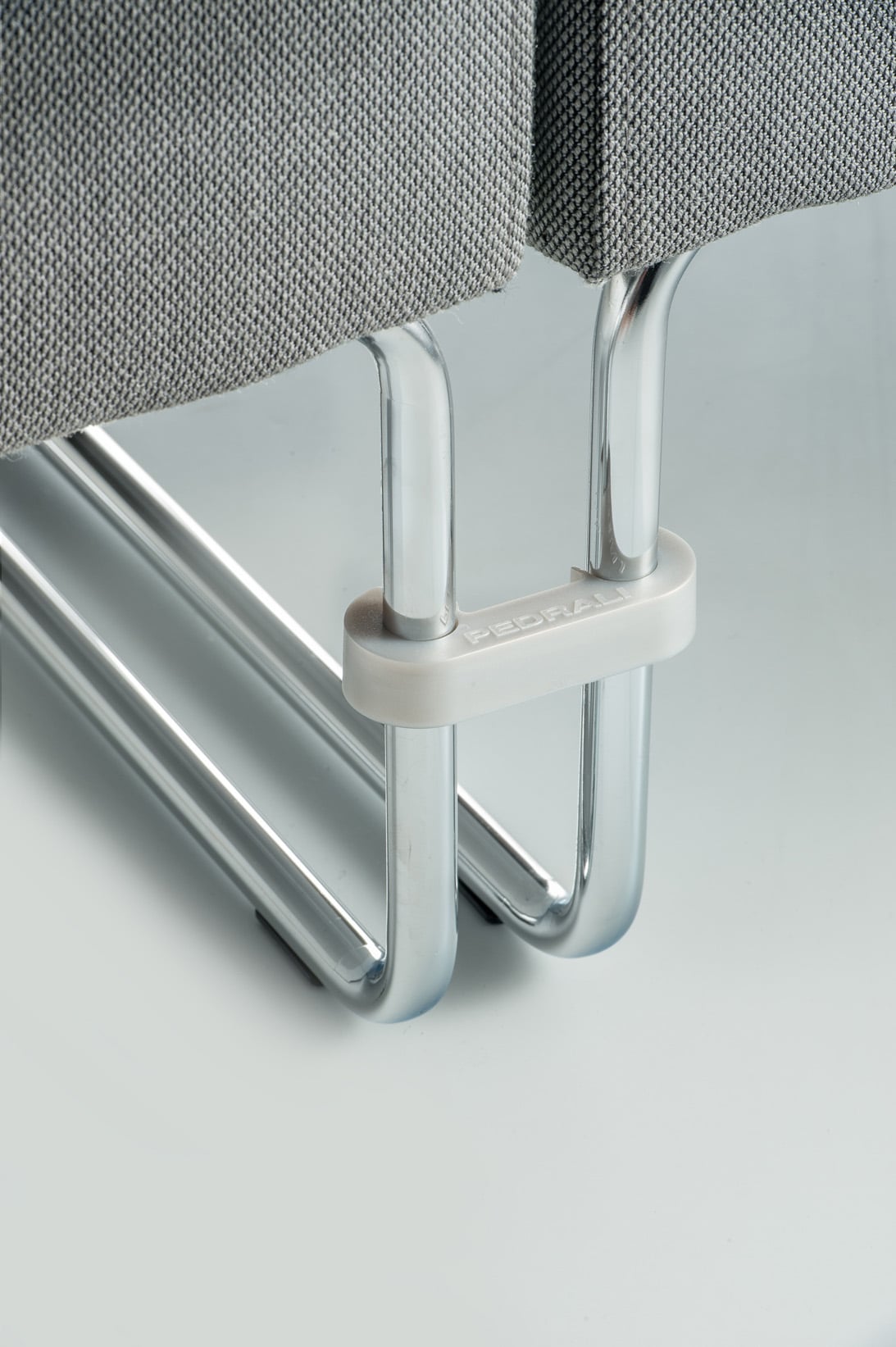host_201203_g63_dettaglio_low Detail des Host Seduta Singula: Kufengestell aus verchromtem Stahlrohr mit Verbindungselement und grauem Stoffpolster.